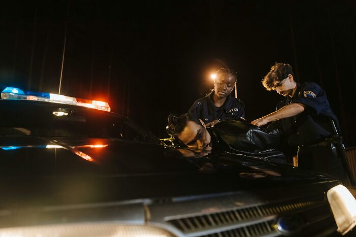 Undercover cops arrest suspect on hood of police car at night.