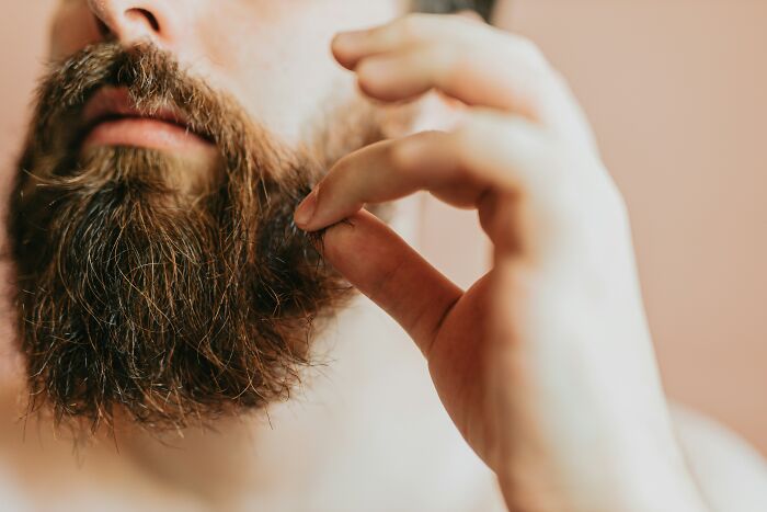 A bearded man adjusts his facial hair, representing undercover cop transformation.