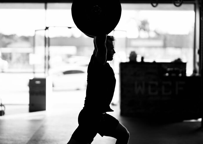 Silhouette of a person lifting weights in a gym setting, demonstrating strength and intensity.