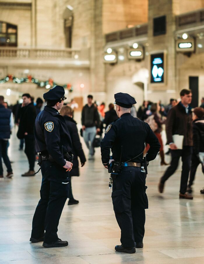 Two undercover cops standing in a busy train station, observing the crowd.