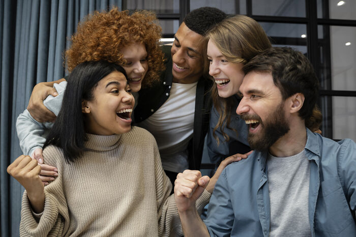 Group of friends sharing an unexpected reality moment, smiling and celebrating joyfully indoors.