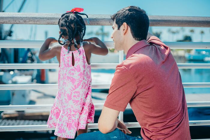 Man and child in a pink dress on a pier, highlighting unexpected things reality offers.
