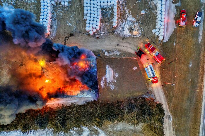 Aerial view of firefighters responding to unexpected blaze, with smoke billowing from a large building in a rural area.
