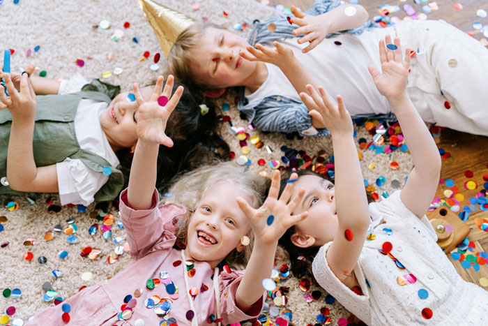Children playing with confetti on the floor, enjoying a party atmosphere indoors.