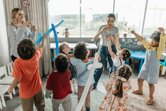 Two women entertaining kids in a lively room, considering ways to uninvite friends' unruly children while keeping friendships intact.
