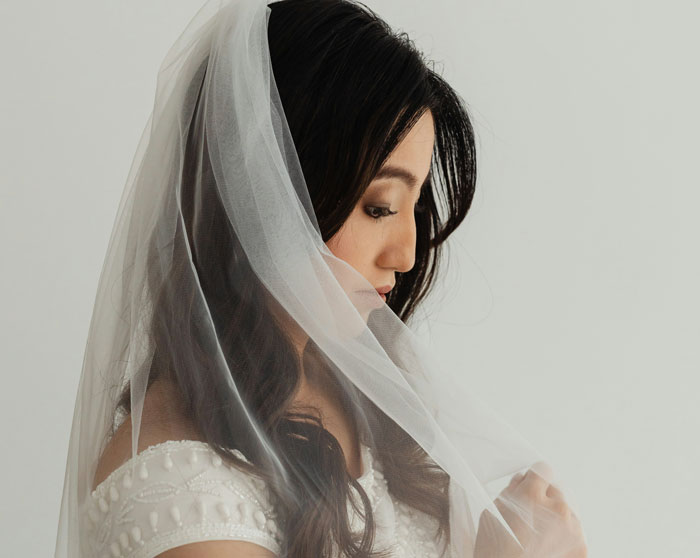 Bride in a white dress and veil thoughtfully touching her veil. Bride in a white dress and veil thoughtfully touching her veil.