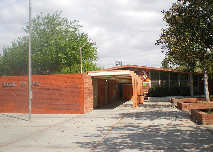 High school entrance with brick walls and trees under a cloudy sky.