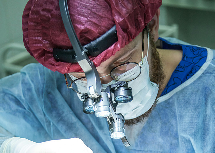 Surgeon focused on a procedure, wearing a mask and magnifying glasses, representing unusual and unsettling facts in medicine.