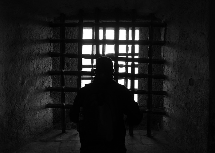 A silhouette of a person with a backpack looks through barred windows, evoking unsettling facts shared by an influencer.
