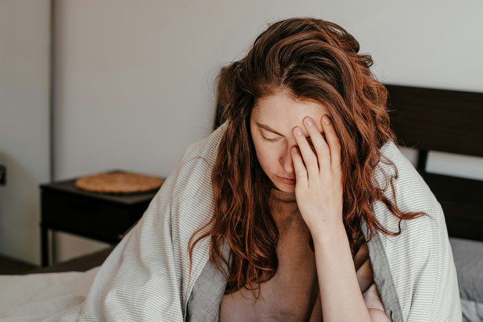 Woman sitting on bed, covering face, wrapped in blanket, looking contemplative, related to coming out story.