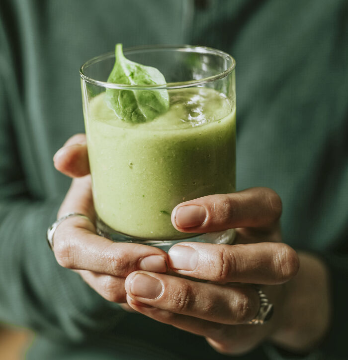 Hands holding a green smoothie with spinach leaf, highlighting misunderstood healthy choices.