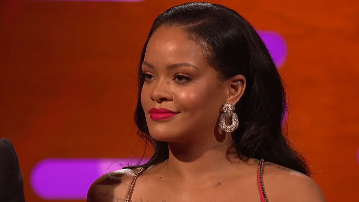 Woman with long hair and pink lipstick, wearing large earrings, in a well-lit studio setting.