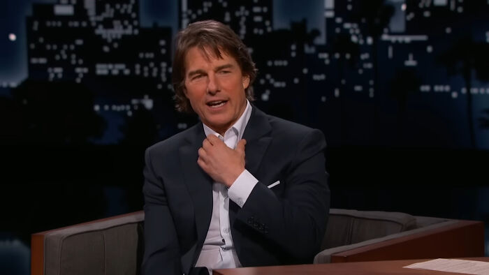 Tom Cruise in a black suit on a talk show, discussing a plausible conspiracy theory.