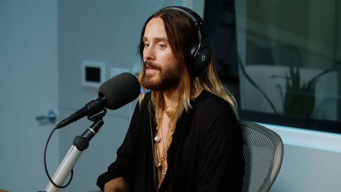 Jared Leto wearing headphones, speaking into a microphone in a studio, related to celebrity conspiracy discussion.