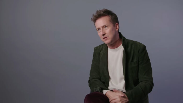 A person in a casual interview setting, wearing a green jacket, discussing celebrity conspiracy theories.