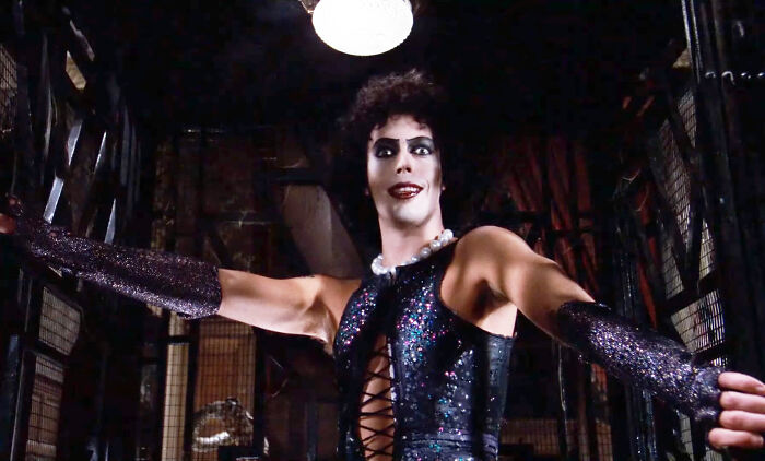 Actor in sparkling costume, open arms, in dimly lit setting, epitomizing a role uniquely their own.