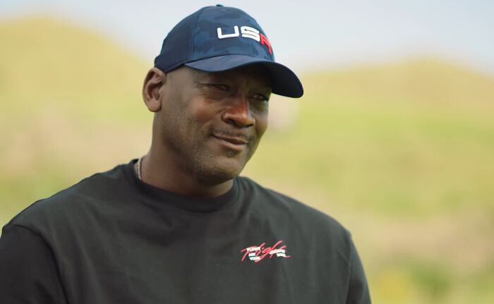 Man wearing a USA cap and black shirt outdoors, related to celebrity conspiracy theme.