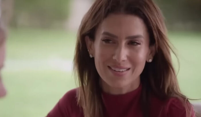Woman in a red top, outdoors, smiling during a conversation, representing a celebrity conspiracy theme.