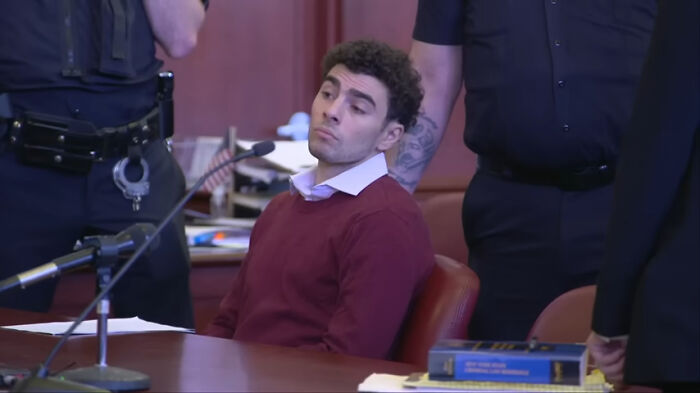 Man in court wearing a red sweater, with officers around, illustrating the concept of "pretty privilege."