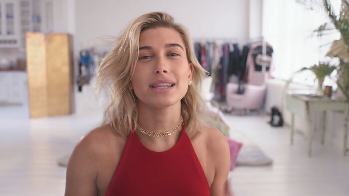 Hayley Bieber in a red top in a well-lit room, possibly linked to celebrity conspiracy theories.