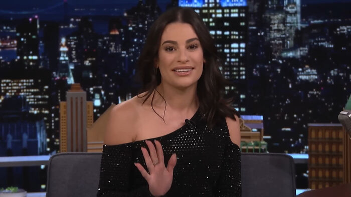 Lea Michelle celebrity waves during a nighttime TV show, discussing a plausible conspiracy theory.