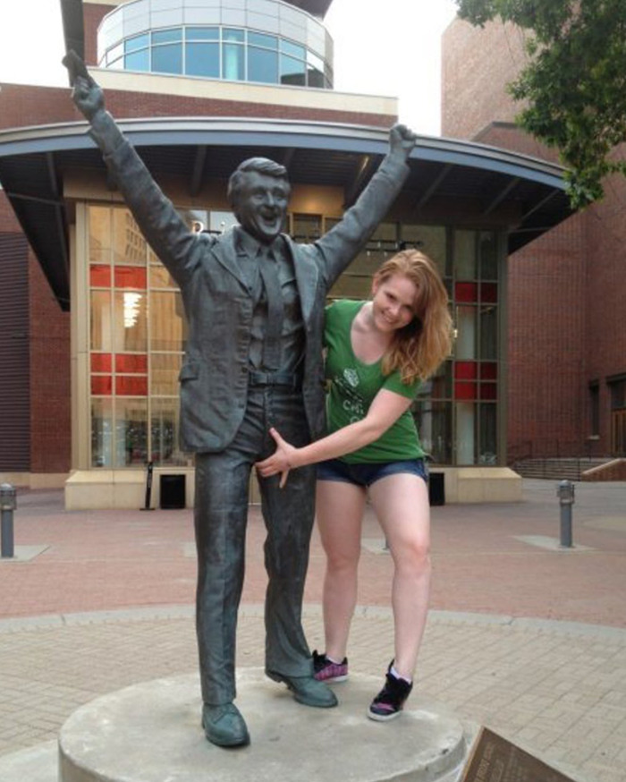 Person posing with a male statue, touching it inappropriately, sparking debate on treating public art respectfully.