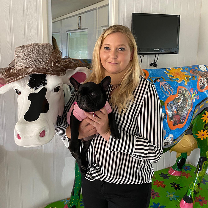 Woman holding a dog stands beside a decorated cow statue, related to Prince Andrew's accuser news.