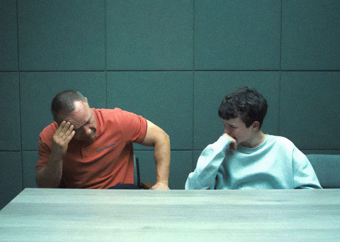 Two people sitting at a table, looking contemplative, related to "Adolescence" TV show's emoji theme.