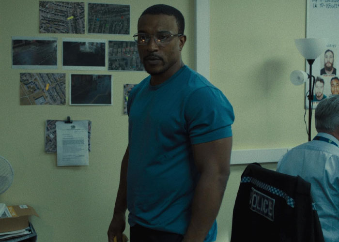 Man in a blue shirt stands in a room with maps and documents, related to TV show "Adolescence" and emoji meanings.