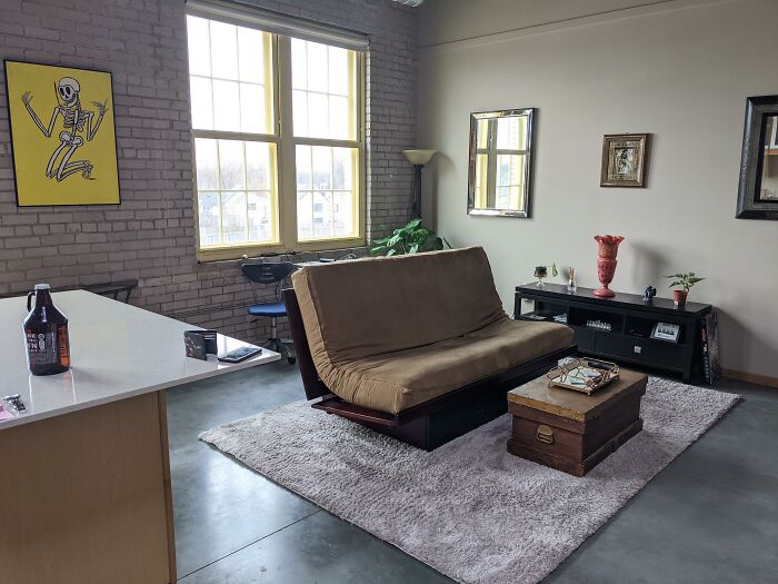 Loft living room with poorly-aging interior design trends featuring a brown futon, vintage decor, and a textured rug.