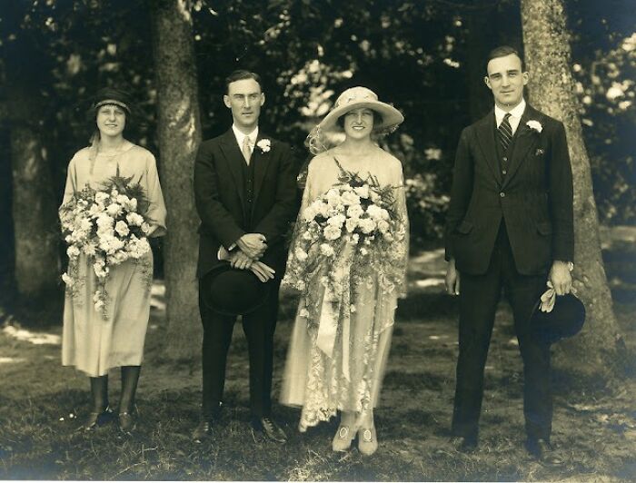 Vintage wedding photo from 50-100 years ago, showing a bride, groom, and attendants with floral bouquets.