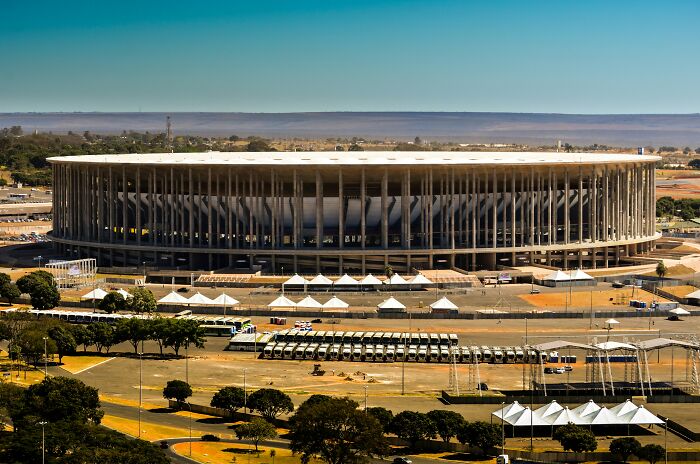 Modern soccer cathedral stadium with large vertical columns and open design under clear blue sky during daytime.