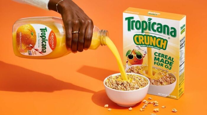 Pouring orange juice over cereal from Tropicana Crunch box, showcasing a weird food combo on an orange background.