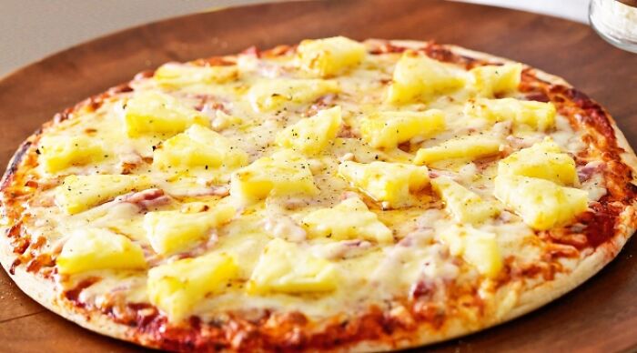 Weird food combo featuring a pizza topped with pineapple chunks on a wooden board.