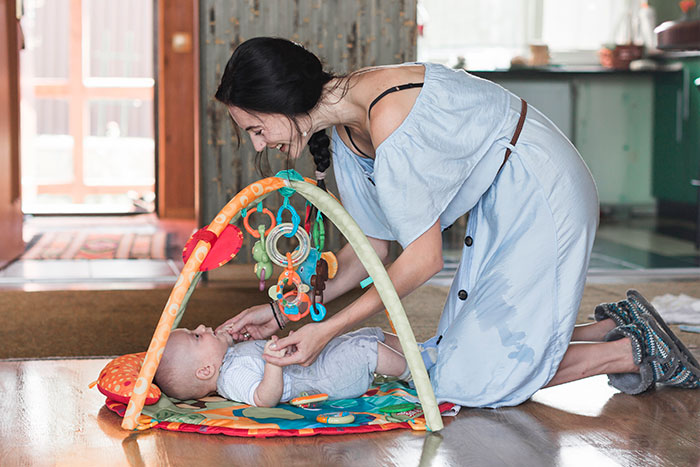 Woman playing with a baby on a colorful play mat in a cozy home setting, highlighting normal USA parenting activities.