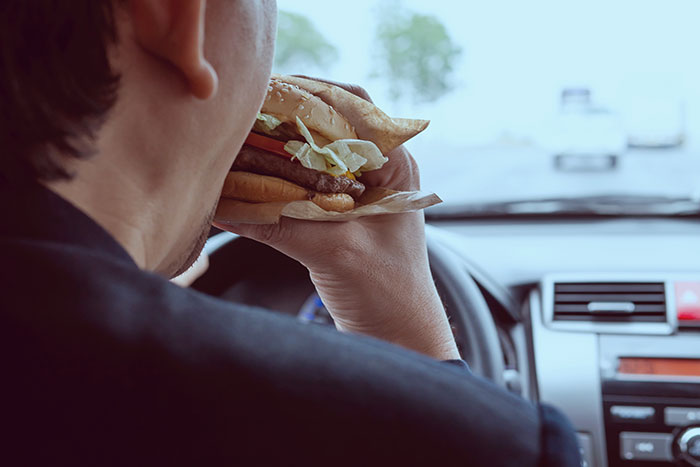 Person eating a hamburger while driving, highlighting a normal activity in the USA.