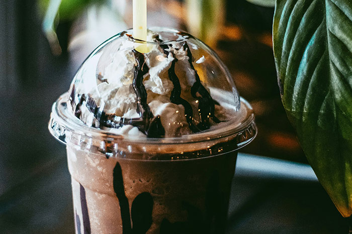 Milkshake with whipped cream and chocolate drizzle in a plastic cup, highlighting American food culture.