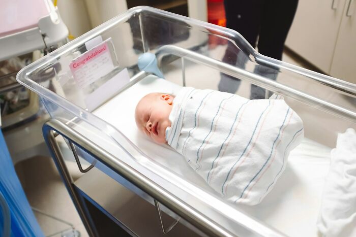 Newborn baby sleeping in a hospital bassinet, wrapped in a striped blanket, possibly associated with family secrets.