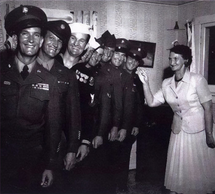 Smiling soldiers and a woman in vintage American home, showcasing everyday life of the past.
