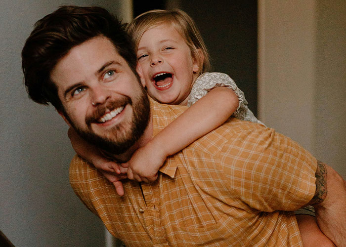 Smiling man giving a piggyback ride to a laughing child, both enjoying a joyful moment at home.