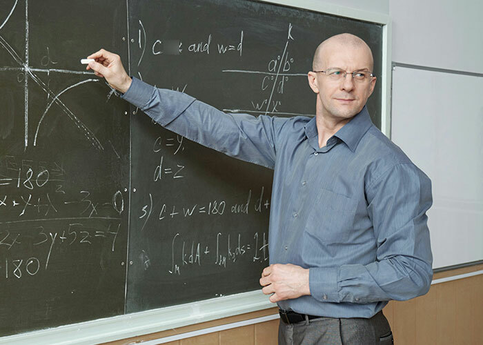 Man in a blue shirt solving equations on a chalkboard, highlighting concepts for the brightest kids.