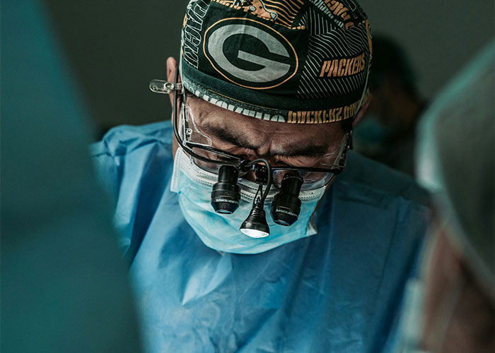 Surgeon in a Green Bay Packers cap, focused during a procedure, representing bright kids' successful careers.
