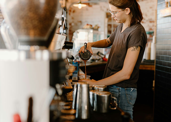 A person with glasses pouring coffee in a cafe, illustrating a successful career path.