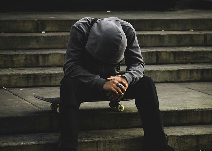 A person in a hoodie sits on steps with a skateboard, head down, representing reflection on bright kids' future.