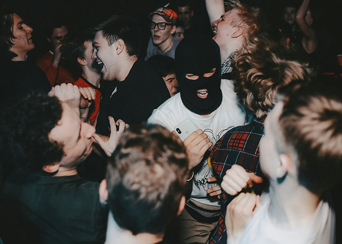 Group of young people dancing energetically, one wearing a black ski mask, at a lively party setting.