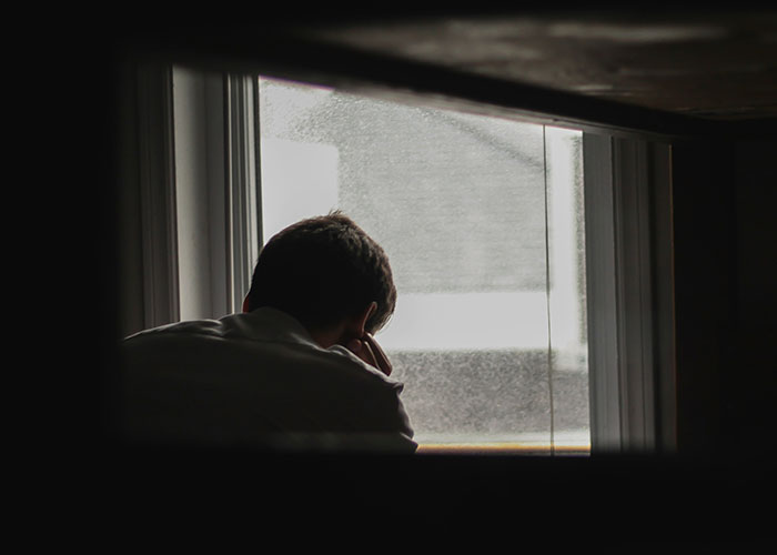 "A person looks thoughtfully out a window, representing brightest kids reflecting on future paths."