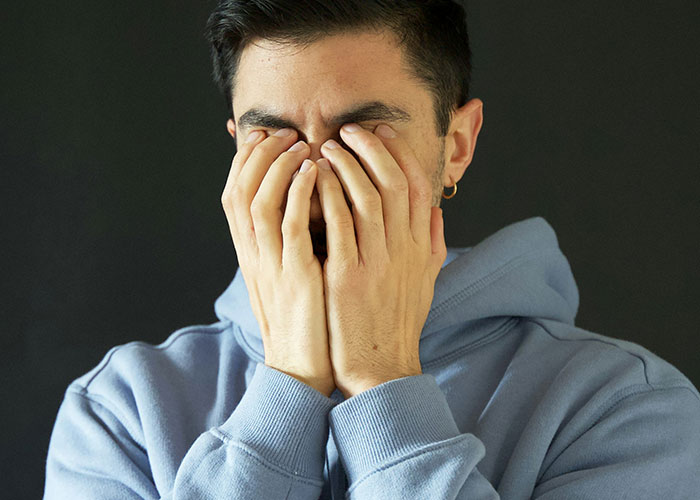 Person in a blue hoodie covering face with hands, expressing emotion.