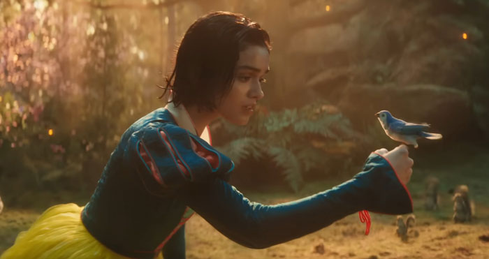 Snow White in the live-action film gently holding a bird in an enchanted forest setting.