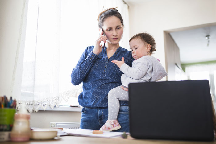 Mom of 3 multitasking, holding child and on phone, in front of a laptop.