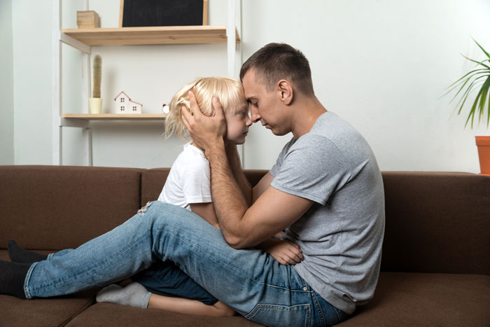 Dad comforting his child on a couch, expressing concern and support during a difficult family situation.